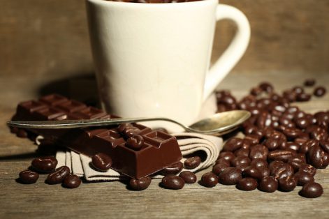 Cup with coffee beans and dark chocolate glaze on wooden background